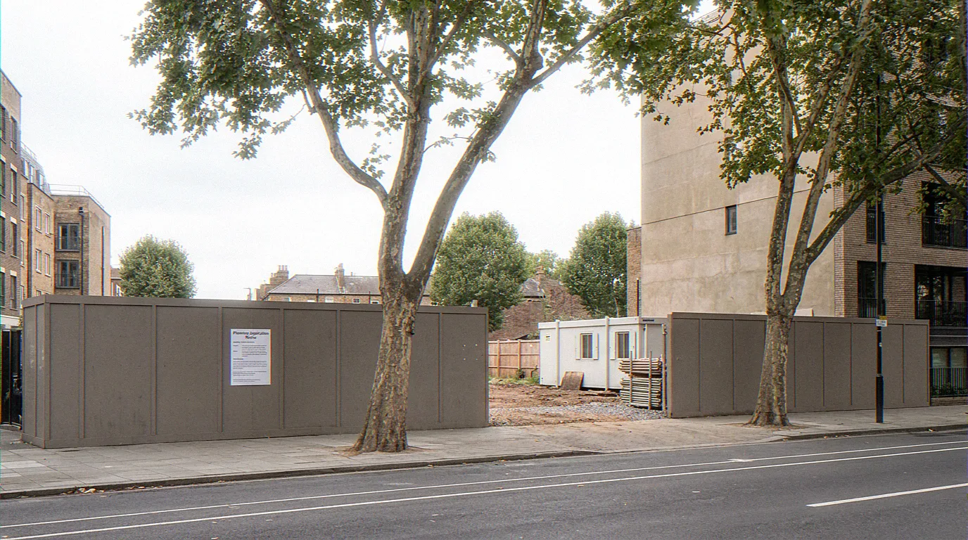 The same London street before construction, with the central plot enclosed by site hoarding